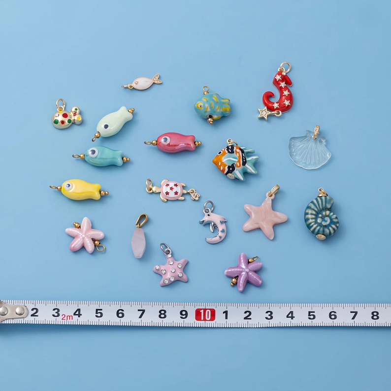 May include: A collection of colorful, nautical-themed charms, including fish, starfish, and seahorses. The charms are in various colors, such as blue, pink, and yellow. A ruler is placed below the charms, with measurements in inches.