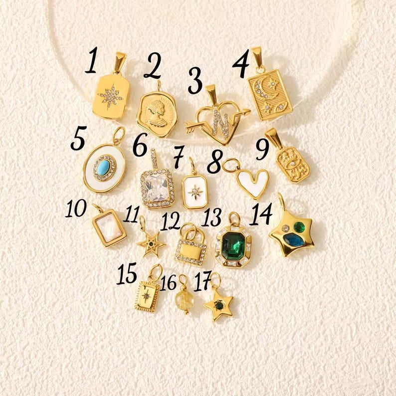 May include: A collection of gold-colored pendants with various designs, including stars, hearts, and geometric shapes. Some pendants feature gemstones and intricate detailing. The pendants are displayed on a cream-colored surface.