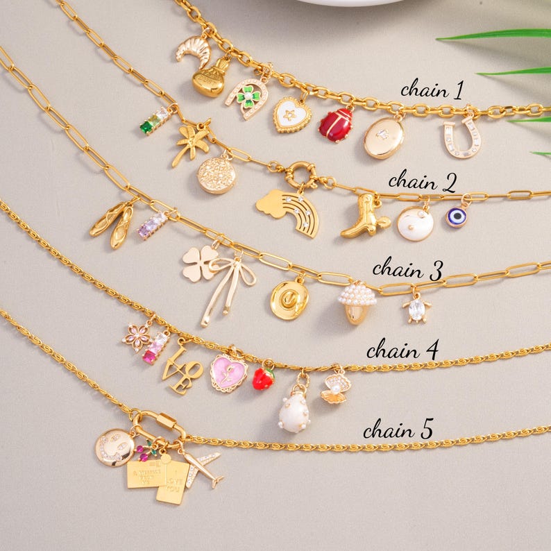 May include: Five gold-colored charm necklaces with various pendants, including a horseshoe, a ladybug, a rainbow, a cowboy hat, and a four-leaf clover. The necklaces are displayed on a light gray surface. The chains are labeled "chain 1" through "chain 5".