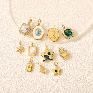 May include: A collection of gold-toned pendants in various shapes, including stars, squares, and ovals. Some pendants feature gemstones in green, blue, and clear, while others have intricate designs. The pendants are displayed on a light-colored surface.