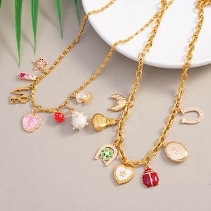 May include: Two gold-colored necklaces with various charms, including a heart, a strawberry, a ladybug, and a horseshoe. The charms are in various colors, including red, white, and pink. The necklaces are on a white plate.