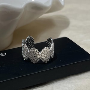 Peut inclure: Une bague en argent avec un design délicat et complexe, présentant de multiples découpes circulaires. La bague est réglable et a un style simple et élégant.
