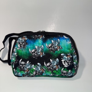 May include: A black zippered bag with a black strap. The bag features a repeating pattern of a cartoon character in shades of blue, white, and brown against a background of green and blue space.