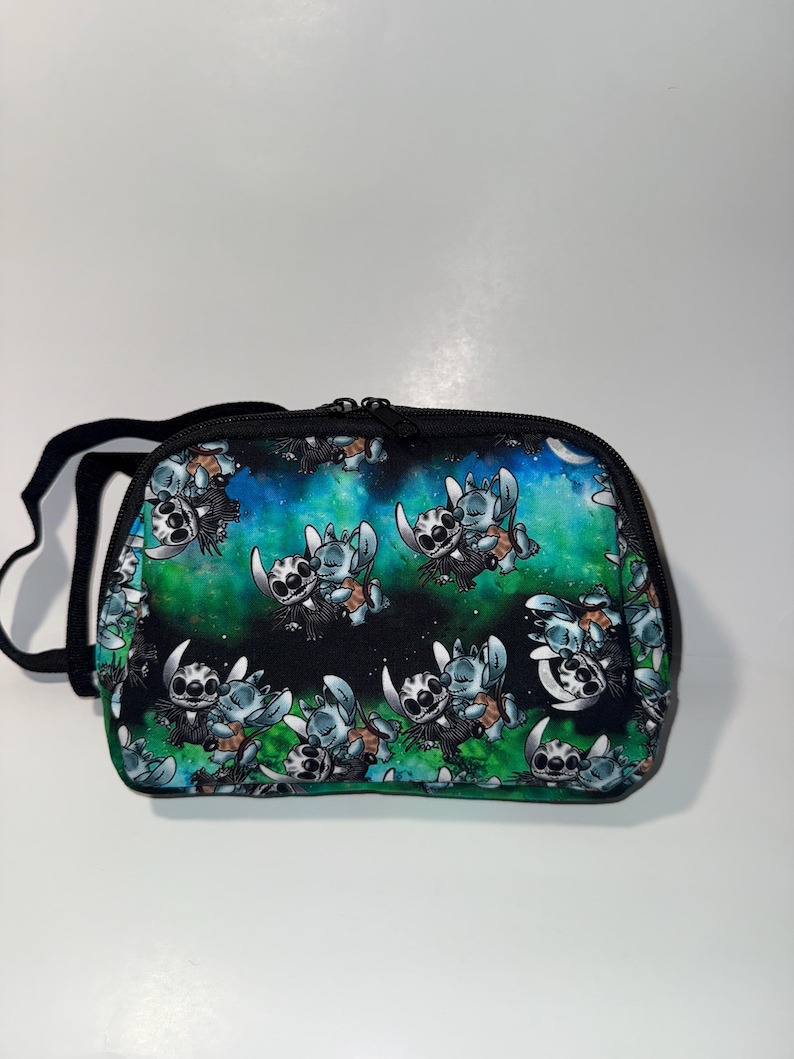 May include: A black zippered bag with a black strap. The bag features a repeating pattern of a cartoon character in shades of blue, white, and brown against a background of green and blue space.