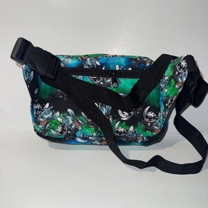 May include: A black fanny pack with a colorful pattern featuring a cartoon character. The bag has a black adjustable strap and a black buckle closure. The background of the pattern is a mix of blue and green.