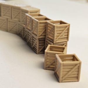 Pode incluir: Uma coleção de pequenas caixas de madeira castanho-claro. As caixas são empilhadas em um arranjo escalonado, com algumas caixas individuais colocadas na frente. As caixas têm um design de ripas com reforços diagonais.