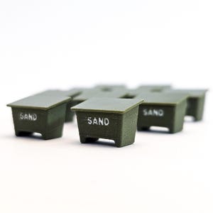 May include: Several small, olive-green containers with the word "SAND" printed in white on the front. The containers have a rectangular shape with a slightly sloped top and four small legs. The background is white.