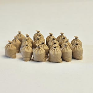 Op de afbeelding: Een verzameling kleine, beige jute zakken, elk aan de bovenkant vastgebonden met een donker touwtje. De zakken zijn dicht bij elkaar geplaatst, waardoor een gestructureerd, repetitief patroon ontstaat. De belichting is zacht.