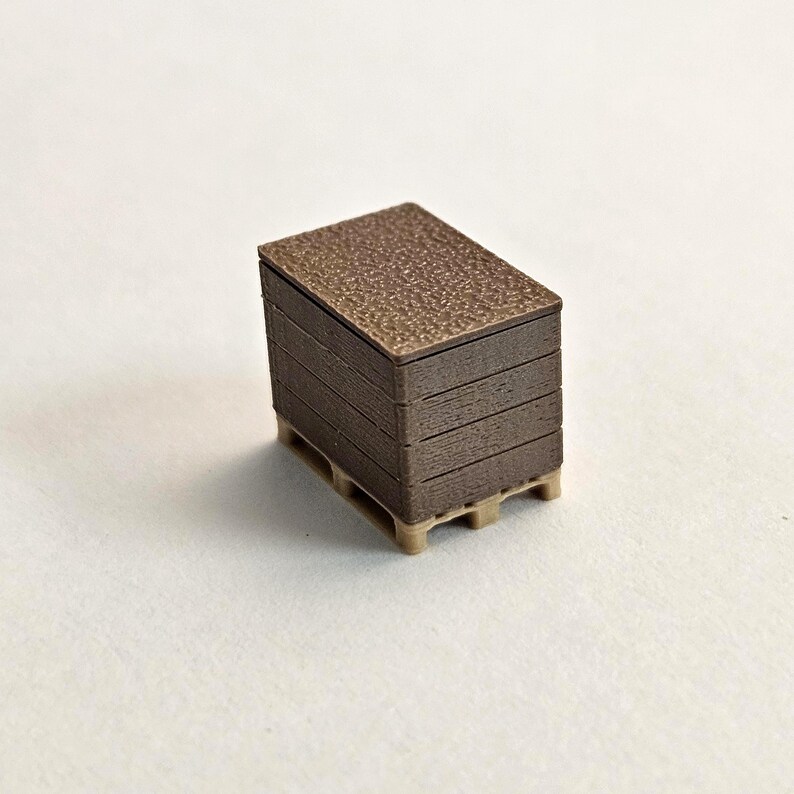 May include: A miniature brown pallet with a stack of brown rectangular objects on top. The top of the stack has a textured surface. The pallet is beige.