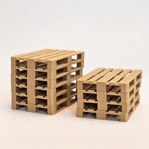 May include: Two stacks of miniature wooden pallets. The pallets are a light brown color and have a rectangular shape with horizontal slats on top. The pallets are stacked on top of each other, creating a three-dimensional effect.