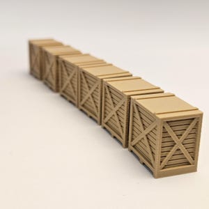 Puede incluir: Una fila de pequeñas cajas de madera de color beige con lados de listones y un diseño en forma de X en la parte delantera. Las cajas están dispuestas en línea, con la más cercana enfocada y las otras borrosas. Las cajas son probablemente para almacenamiento o exhibición en miniatura.