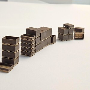 May include: Miniature brown wooden crates and pallets are stacked in various configurations. The crates are rectangular with open tops, and the pallets have a slatted design. The scene suggests a warehouse or storage setting.