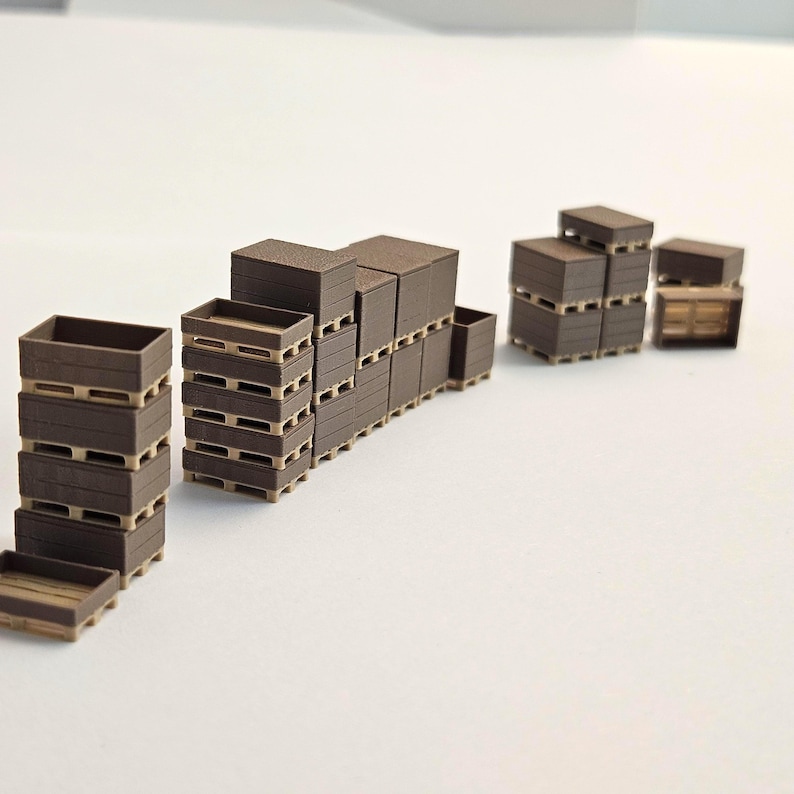May include: Miniature brown wooden crates and pallets are stacked in various configurations. The crates are rectangular with open tops, and the pallets have a slatted design. The scene suggests a warehouse or storage setting.