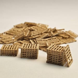 Peut inclure: Une collection de petites palettes en bois brun clair. Plusieurs piles de palettes miniatures sont au premier plan, avec un plus grand tas de palettes individuelles en arrière-plan. Les palettes sont faites de fines lattes de bois.