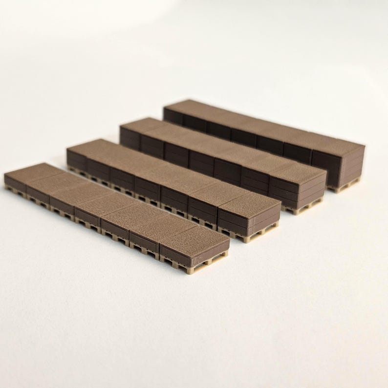 May include: Four brown rectangular miniature pallets are arranged in a diagonal line. The pallets have a textured surface and are stacked in varying heights. The pallets are made of a dark brown material and have a light brown base.
