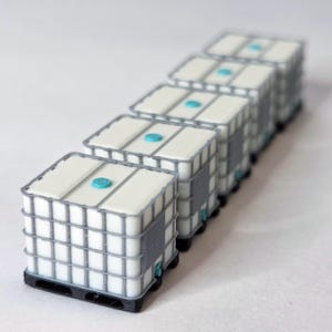 Puede incluir: Una fila de contenedores intermedios a granel (IBC) en miniatura blancos y grises con detalles en azul. Cada contenedor tiene una parte superior blanca con una tapa azul, una jaula gris y una base de paleta negra. Los contenedores están alineados.