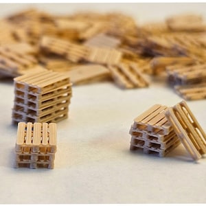 May include: A collection of miniature wooden pallets, in various arrangements. The pallets are light brown and have a classic slatted design. Some are stacked, while others are scattered, suggesting a small-scale construction or model-making project.