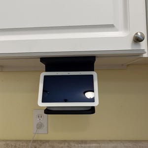 Peut inclure: Support noir sous l'armoire tenant un écran intelligent blanc avec un écran noir. L'écran est monté sous une armoire blanche. Une prise électrique blanche est visible sur le mur.