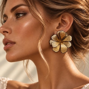May include: A large, dimensional flower-shaped earring featuring metallic gold petals with a textured, beaded surface and thin black outlines, worn on the earlobe to create a bold, statement-making accessory piece.