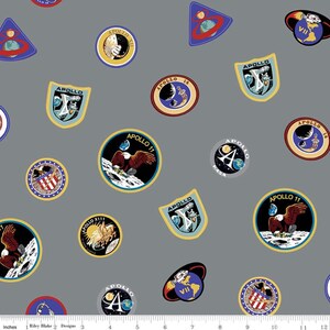 May include: A gray fabric with a repeating pattern of colorful NASA Apollo mission patches. The patches feature the words "Apollo" and Roman numerals, along with images of the moon, an eagle, and the American flag.
