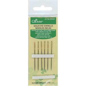 May include: A pack of six Clover Gold Eye Chenille needles, size No. 20, displayed on a light green card with white clover patterns. The needles feature metallic gold-colored eyes and are held in place by two horizontal white strips.