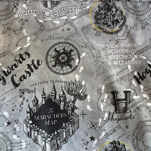 May include: A gray and black fabric with a repeated pattern of a map of Hogwarts Castle, the Marauder's Map, and the Hogwarts crest. The text "Hogwarts School of Witchcraft & Wizardry" is also included in the pattern.