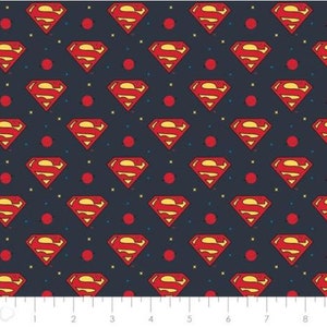 May include: A navy blue fabric with a repeating pattern of red Superman logos and small red circles. The fabric has a subtle yellow and white speckled pattern.
