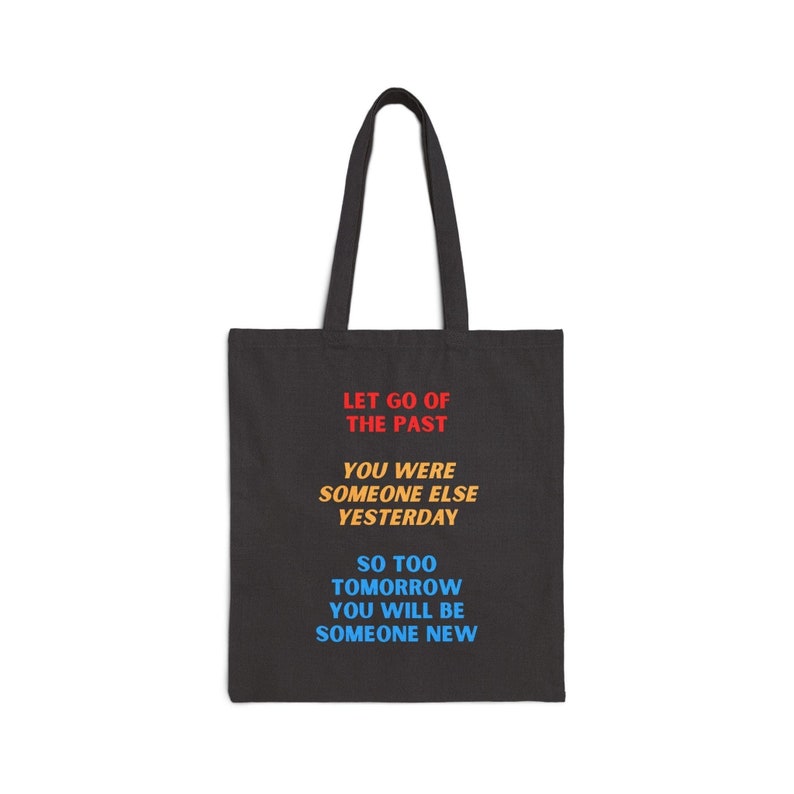 Black tote bag that reads, in primary colors (red, yellow, and blue, in that order): LET GO OF THE PAST // YOU WERE SOMEONE ELSE YESTERDAY // SO TOO TOMORROW YOU WILL BE SOMEONE NEW