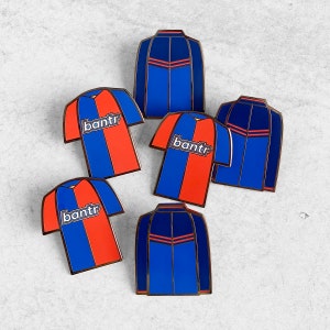 May include: Six enamel pins featuring a blue and red soccer jersey design with the word "bantr" on the front. The pins are arranged in a semi-circle on a white background.