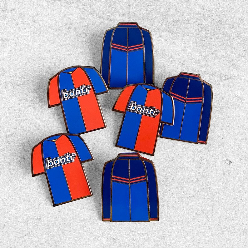 May include: Six enamel pins featuring a blue and red soccer jersey design with the word "bantr" on the front. The pins are arranged in a semi-circle on a white background.