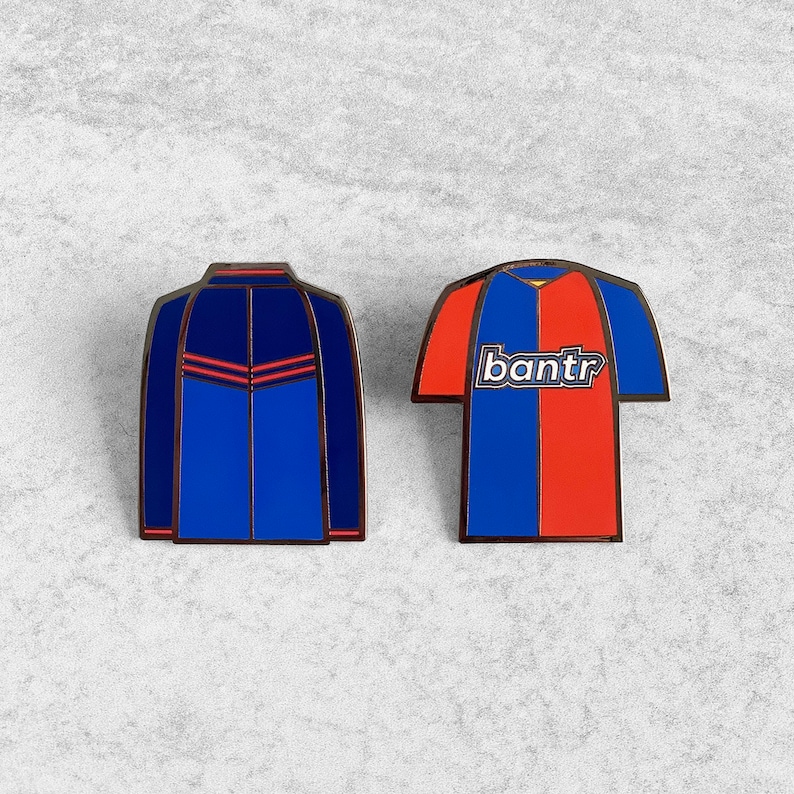 May include: Two enamel pins featuring a blue and red soccer jersey with the word "bantr" on the front and a blue jacket with red accents.