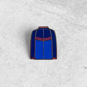 May include: Blue enamel pin with red accents depicting a jacket with a zipper and a V-shaped design on the front.