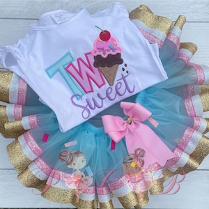 May include: A white onesie with the words "Two Sweet" and an ice cream cone graphic. The onesie is paired with a blue tulle tutu with pink and gold ribbon trim.