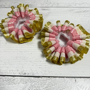 May include: Two pink, white and gold glitter hair bows with ruffled edges.