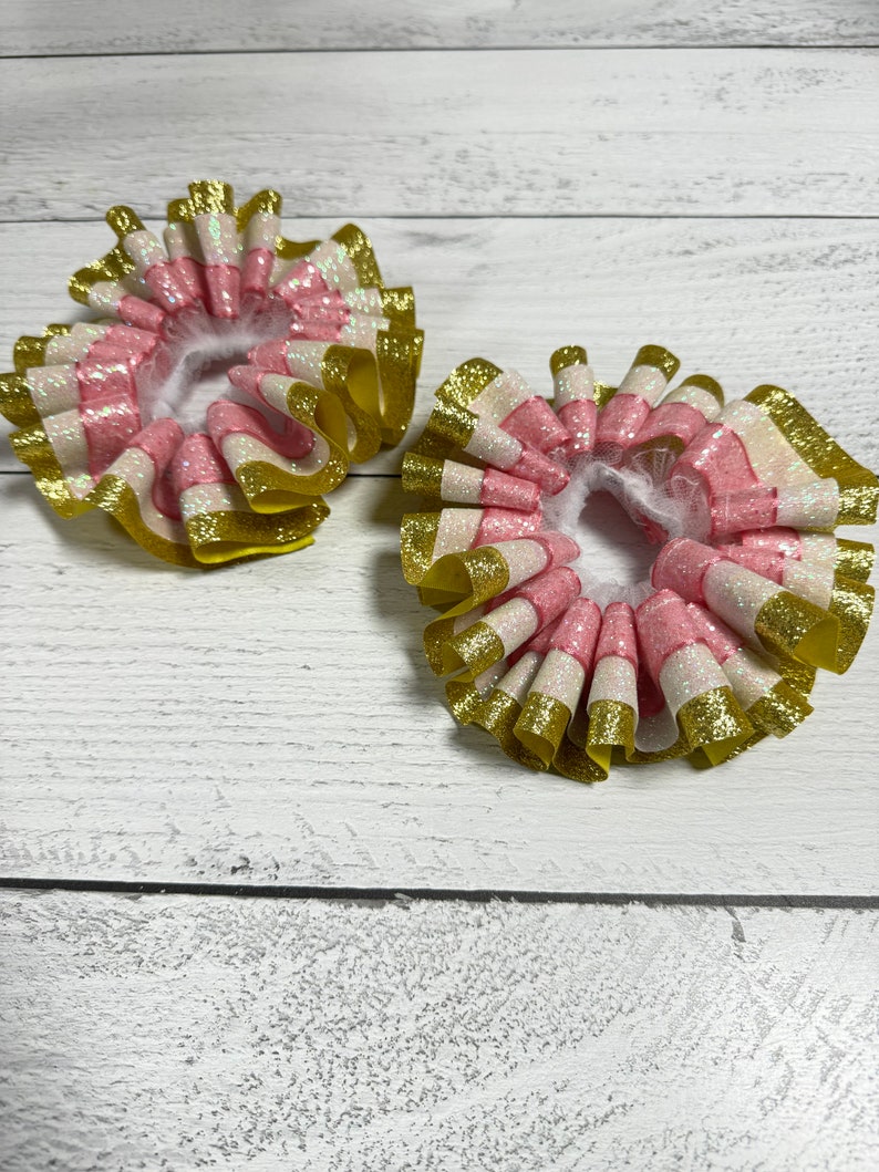May include: Two pink, white and gold glitter hair bows with ruffled edges.