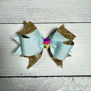 May include: A light blue bow with gold glitter accents and a pink, purple and green ice cream cone charm.