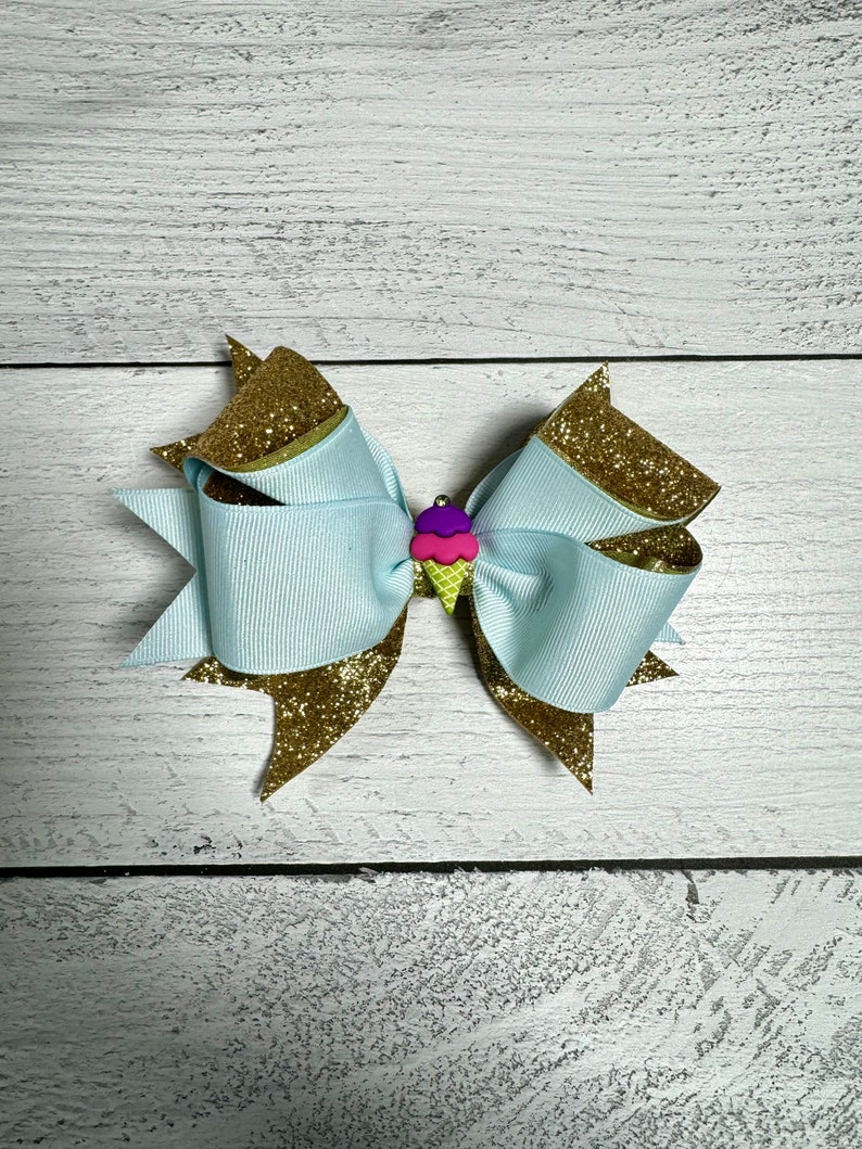 May include: A light blue bow with gold glitter accents and a pink, purple and green ice cream cone charm.