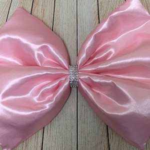 Könnte beinhalten: Eine große rosa Schleife aus Satin mit einem silbernen Strassstein-Verzierungen in der Mitte.