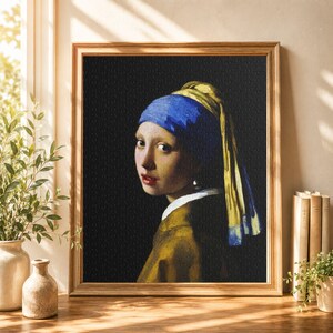 以下が含まれることがあります： 真珠の耳飾りの少女の絵画が描かれた額縁入りのジグソーパズル。被写体は青いターバンに黄色い布の垂れ飾り、茶色の服を身につけ、真珠の耳飾りを付けており、背景は無地の黒で、木製のフレームに収められています。