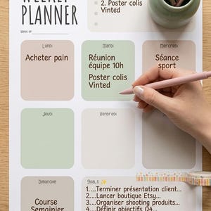 Peut inclure: Une feuille de planning hebdomadaire sur fond blanc, avec des cases de couleurs pastel pour chaque jour de la semaine. Le planificateur comprend des sections pour une liste de tâches et des objectifs, avec du texte manuscrit et du ruban adhésif décoratif.