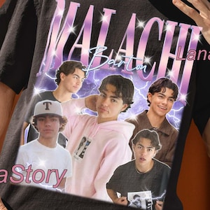 May include: Black unisex t-shirt with a graphic of a person and the text "MALACHI Barton" in a purple and white design. The shirt also has the text "UNISEX T-SHIRT" at the top. The Lana Story logo is visible on the shirt.