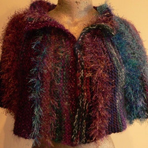 May include: A purple, green, and blue striped knitted shawl with a fuzzy texture.