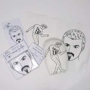 May include: A black and white sewing kit to make a George Michael doll. The kit includes a pattern, fabric, and instructions. The doll is wearing a shirt that says "Choose Life".