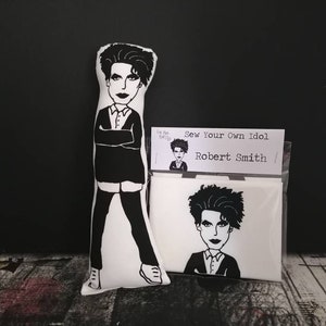 May include: A black and white illustration of Robert Smith, the lead singer of The Cure, on a white fabric pillow. The pillow is part of a kit to sew your own idol.