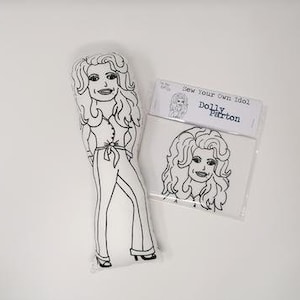 Peut inclure: Un dessin au trait noir et blanc de Dolly Parton sur un oreiller blanc. L'oreiller est prêt à être colorié. Le texte "Cousez votre propre idole Dolly Parton" est sur une carte blanche.