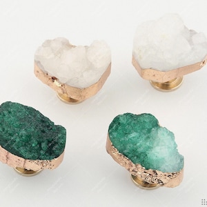May include: Four cabinet knobs with a crystal-like design. Two are white, two are green, each with a gold-coloured metal base and trim. These knobs offer a natural aesthetic for furniture, adding a unique touch.