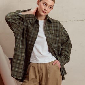 Op de afbeelding: Een vrouw draagt een groen en wit geruit flanellen overhemd over een wit t-shirt en een kaki broek.