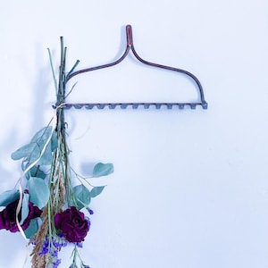May include: A dark metal wall-mounted floral hanger with a bouquet of dried flowers. The bouquet includes deep red roses, purple statice, and eucalyptus leaves. The hanger is a dark reddish-brown color.