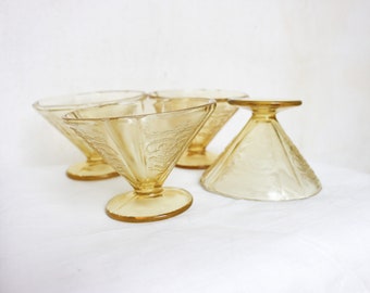 May include: Four vintage amber-colored dessert glasses. Each glass features a triangular bowl with etched floral patterns and a round base. One glass is inverted, showcasing the base and the etched design.
