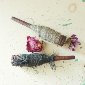 May include: Two wooden spools of thread, one with beige thread and one with black thread. A dried rose is also in the image.